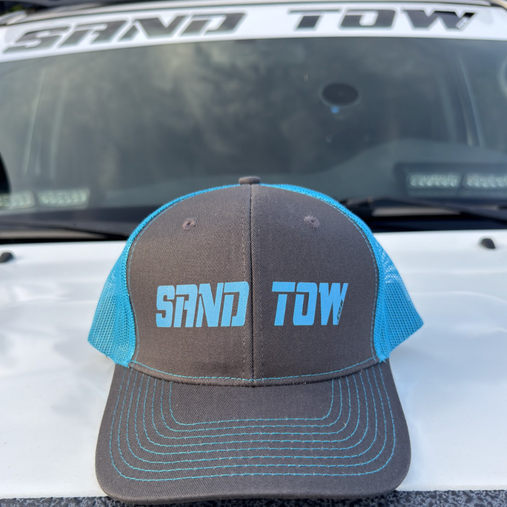 Gray cap with blue mesh and 'SAND TDW' text on a vehicle's open trunk.